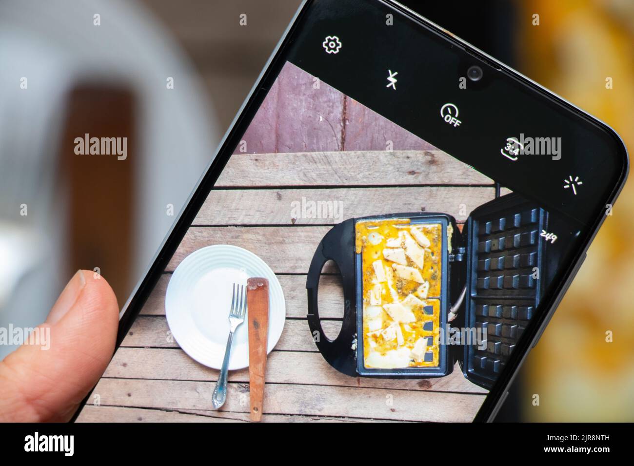 fry scrambled eggs with cheese and spices in a waffle iron on a wooden background, boil scrambled eggs in a waffle iron from the phone screen Stock Photo