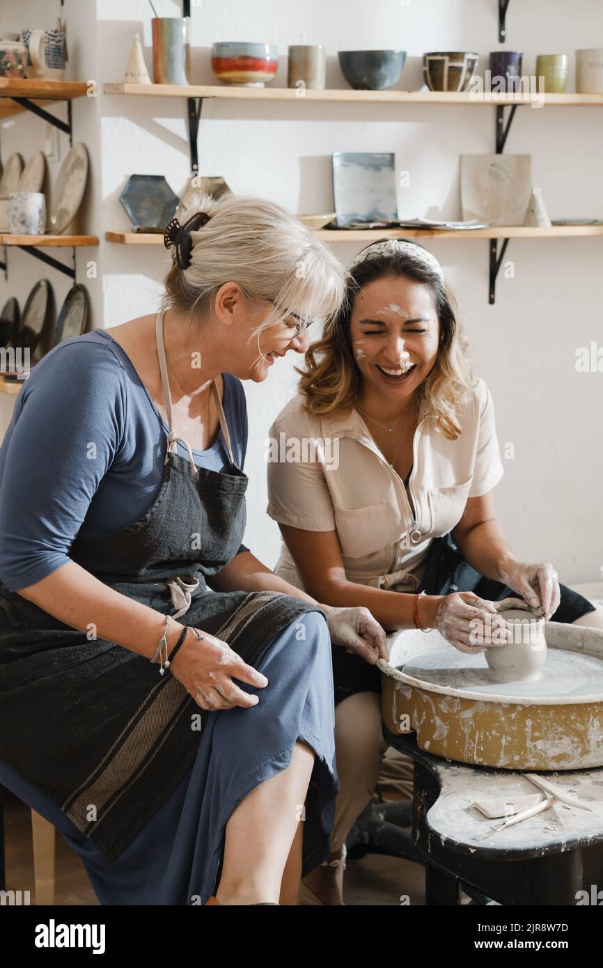 Teacher and student at pottery workshop learning to make bowls from clay. Happy woman doing handmade dishes. Lesson for adults at ceramics studio Stock Photo