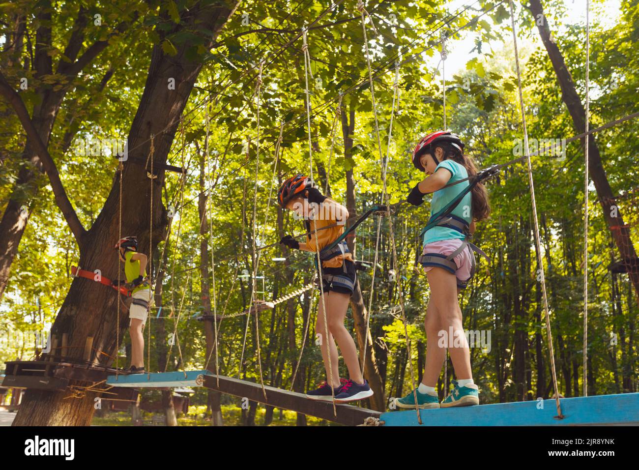 The little children in protective helmets step on the suspension bridge and hold on to the ropes Stock Photo