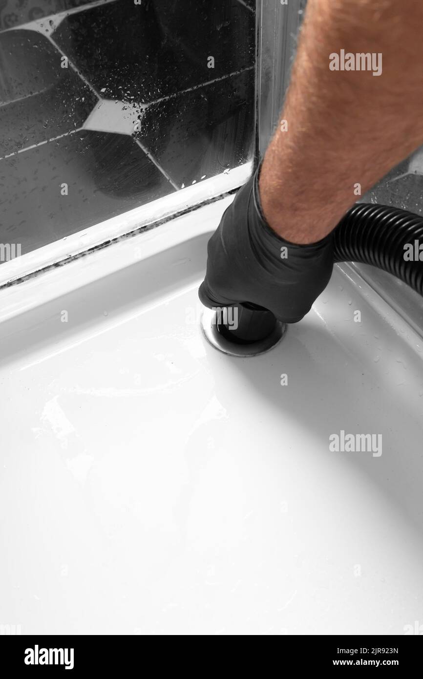 Man unblocking pipes in a bathroom shower cubicle using a hoover. Do it
