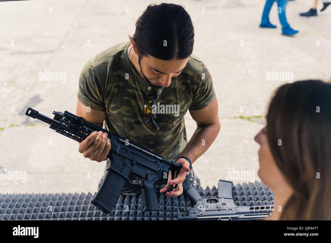 Handsome dark-haired muscular adult caucasian man in a moro t-shirt looking at a black gun at the reseller's place. Outdoor shot. High quality photo Stock Photo