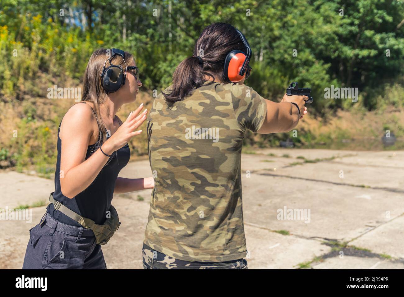Two Europeans at a shooting range. Private shooting lessons. Female instructor and a man in moro t-shirt. Aiming at target. Outdoor shot. High quality photo Stock Photo