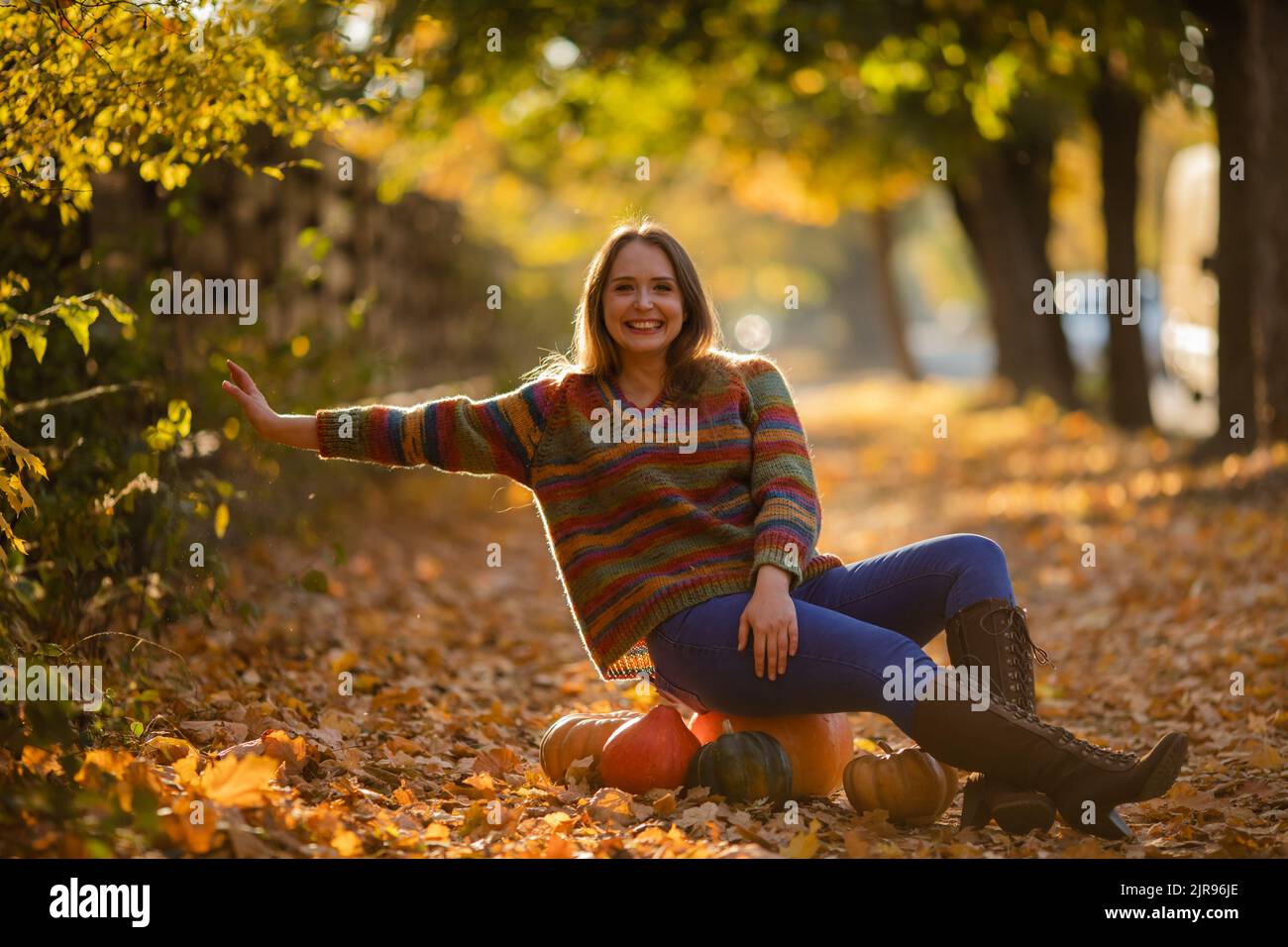 Smile woman sitting on the pumpkin on the autumanl maple leaves. Cozy autumn vibes Halloween, Thanksgiving day. Stock Photo