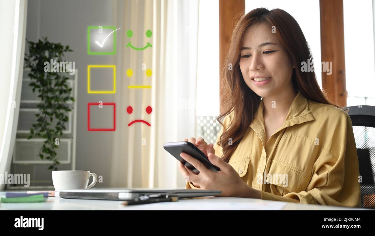 Beautiful young woman using mobile phone, giving satisfied rating with ...