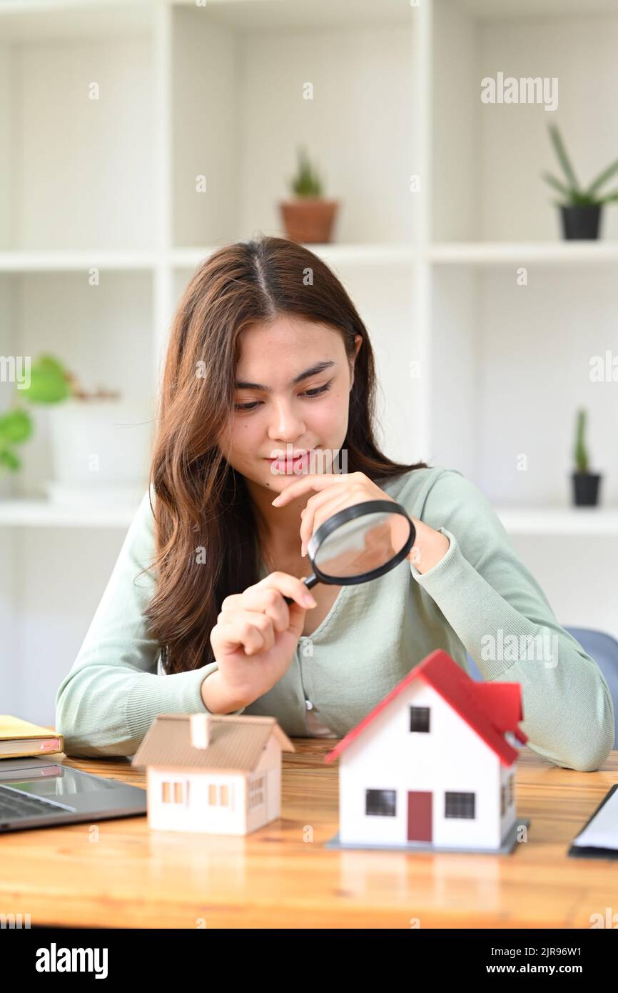 Young woman appraiser with magnifying glass looking at house models
