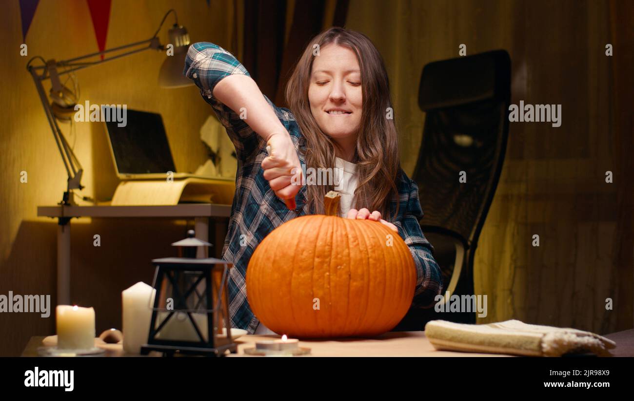 Preparing pumpkin for Halloween. Woman sitting and carving with knife halloween Jack O Lantern pumpkin at home for her family. Stock Photo