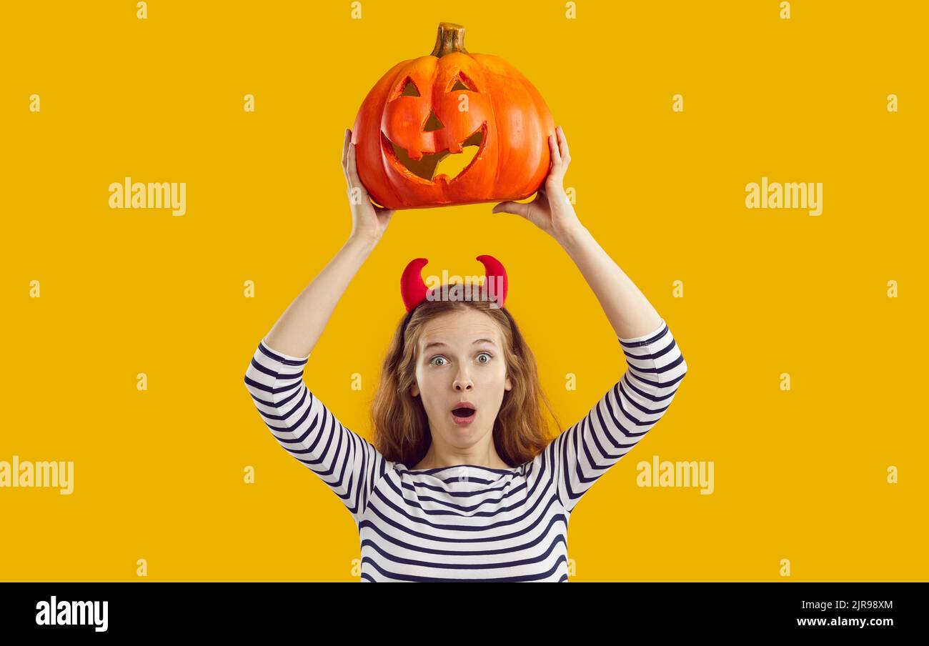 Studio portrait of woman with funny surprised face expression holding up Halloween pumpkin Stock Photo