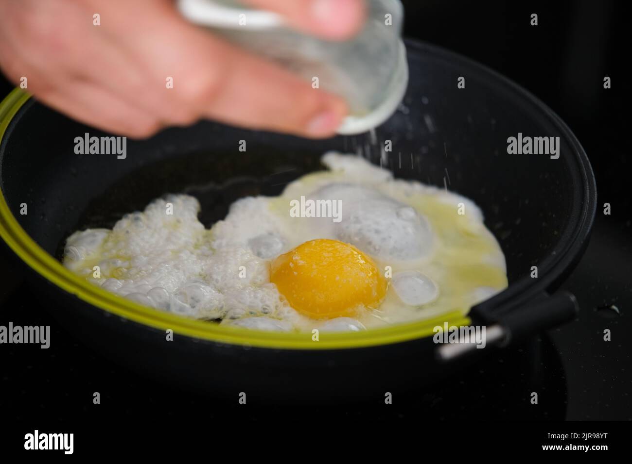 Male hand adding salt to egg in frying pan. Stock Photo