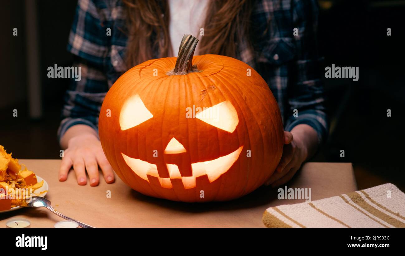 Illuminated pumpkin for Halloween. Woman sitting and showing out candle lit halloween Jack O Lantern pumpkin at home for her family. Stock Photo