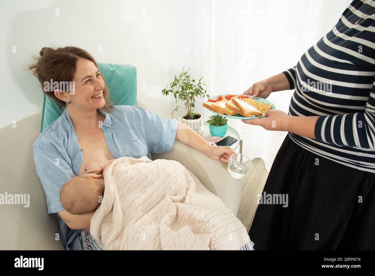 Elder woman helps to eat for new mother when she breastfeeds her baby. Motherhood support Stock Photo