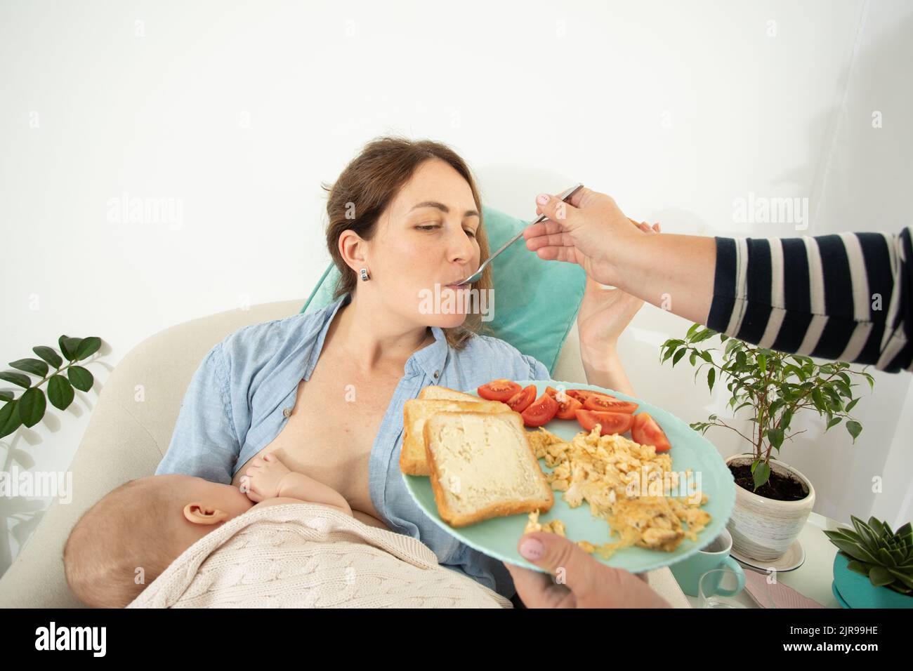 Elder woman helps to eat for new mother when she breastfeeds her baby. Motherhood support Stock Photo