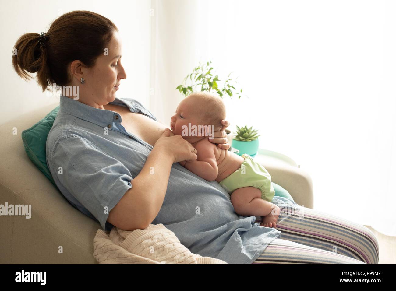 Breastfeeding in laid back position. Mothed and baby at the chair. Stock Photo