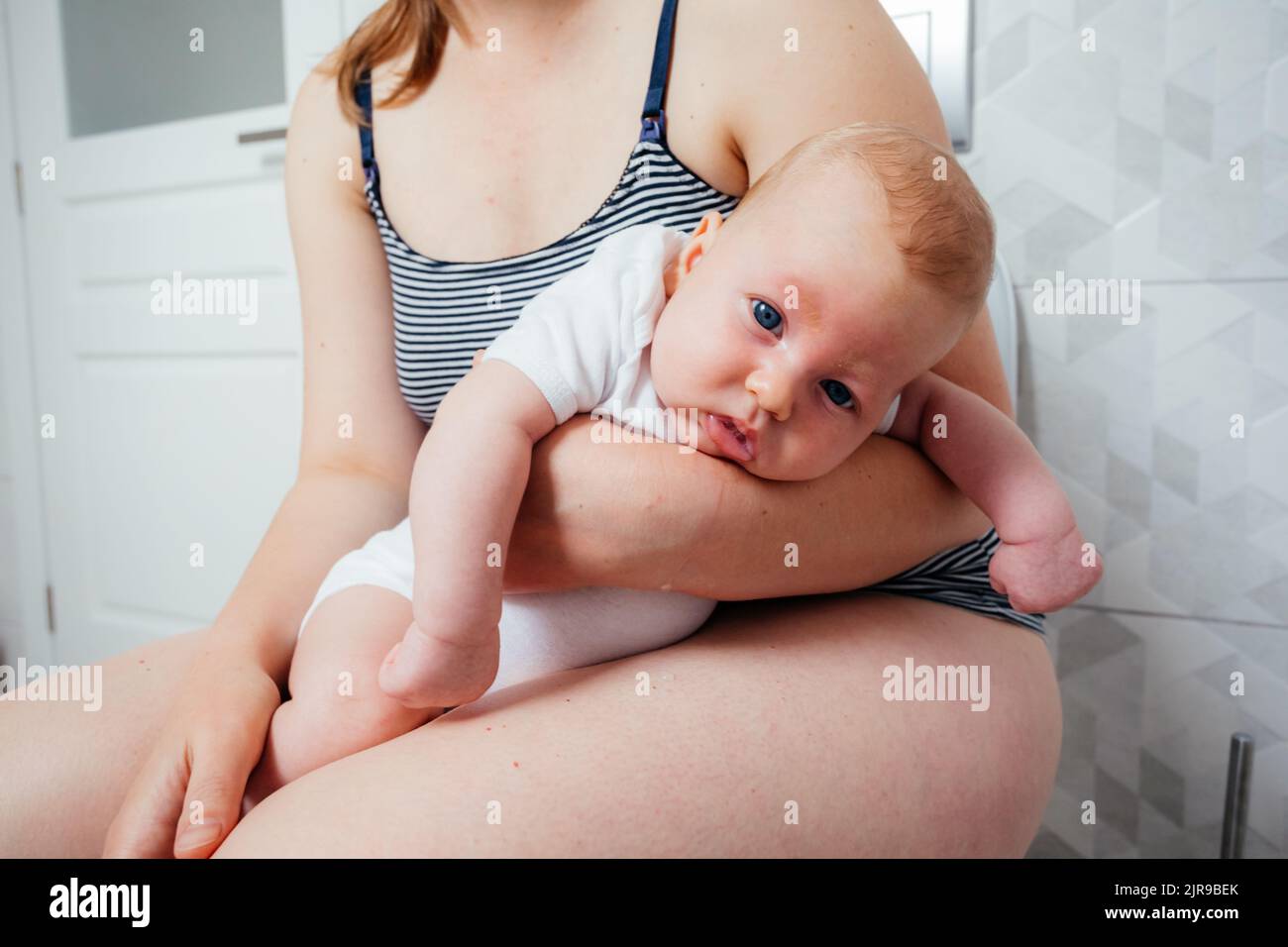 Tired depressed mother with crying newborn baby sitting on the lavatory pan Stock Photo