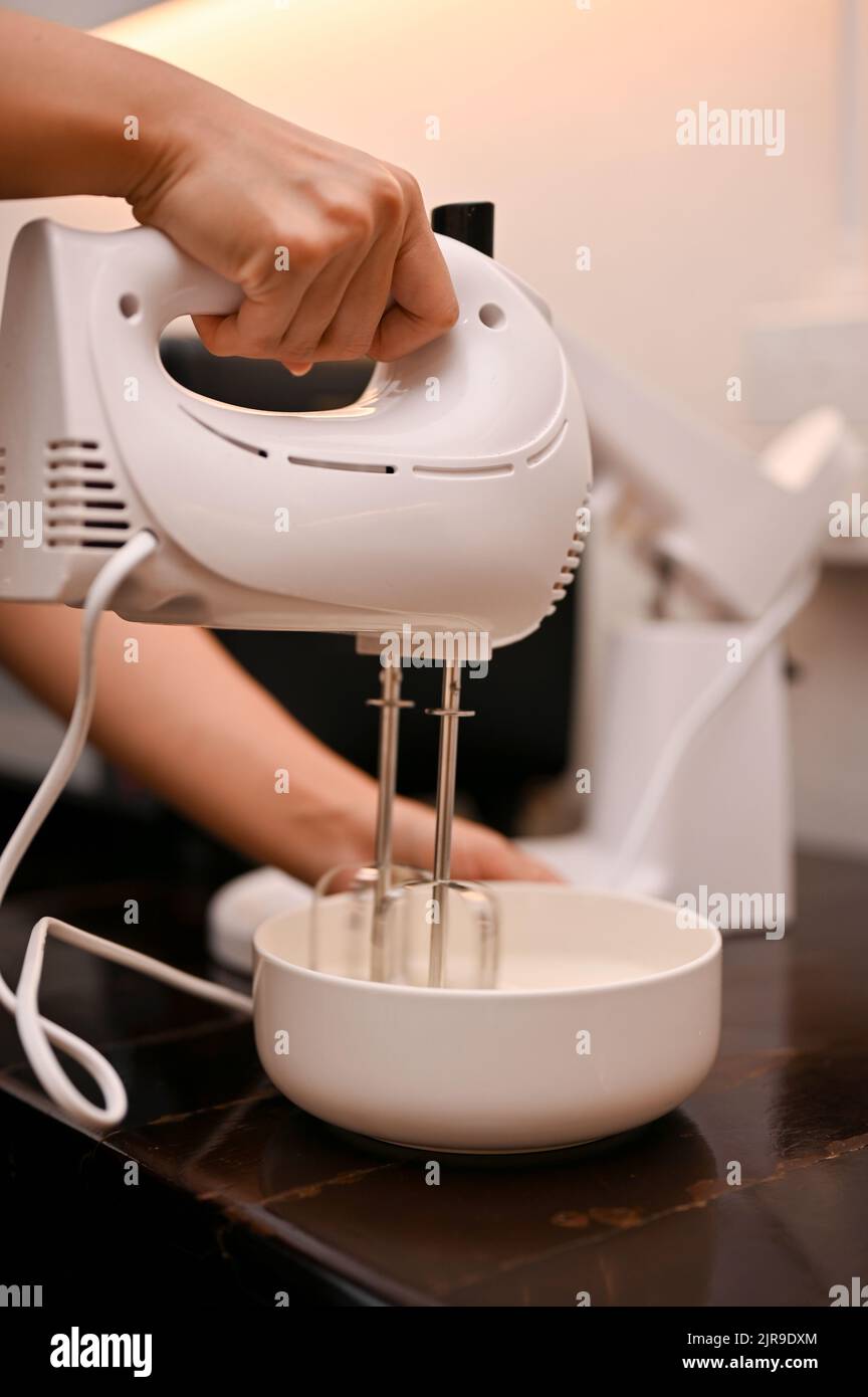 A female baker beat the eggs, sugar, and flour in a mixing bowl with a
