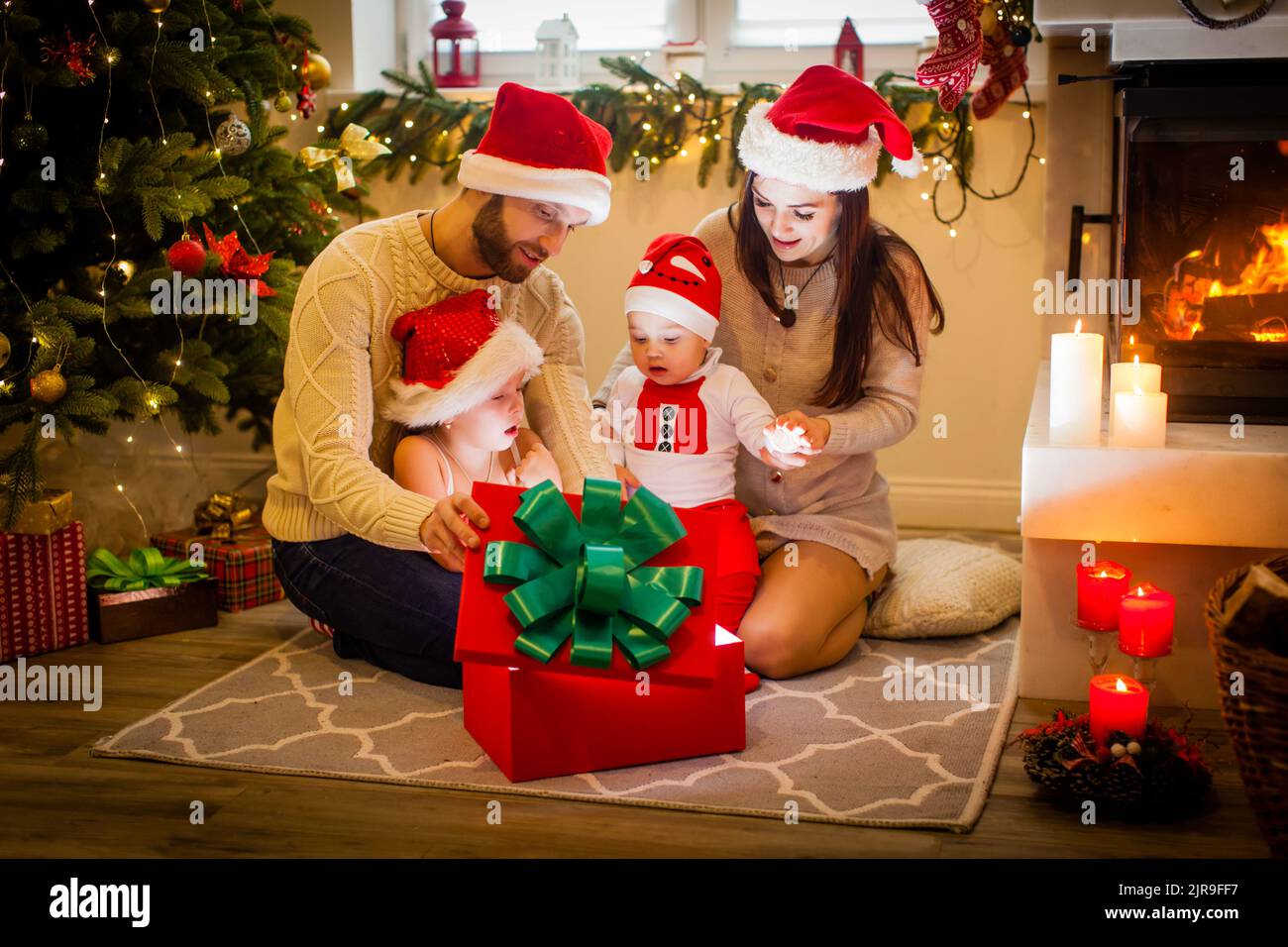 Happy family mother father and children with magic gift near tree near the fireplace at Chriasmtas time Stock Photo