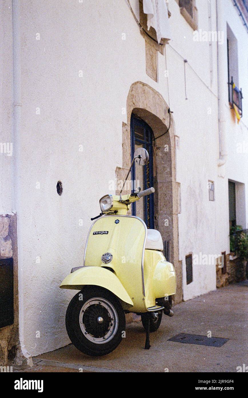 A vertical shot of Italian yellow Vespa scooter parked in front of a white building Stock Photo