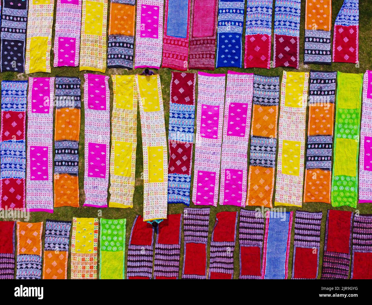 Narayanganj, Dhaka, Bangladesh. 23rd Aug, 2022. Colorful strips of fabric produce an eye-catching display as they are laid out in neat rows across a field in Narayanganj, Bangladesh. Locally called ''Saree'' - a traditional clothing garment for women, the long cotton cloths are set out to dry under the hot sun, having been dyed with bright colours. About 4000 pieces of cloth are laid to dry here everyday. The process usually takes three hours, with each set of 200 pieces at a time to dry in temperatures that can reach over 36 degrees celsius. Credit: ZUMA Press, Inc./Alamy Live News Stock Photo