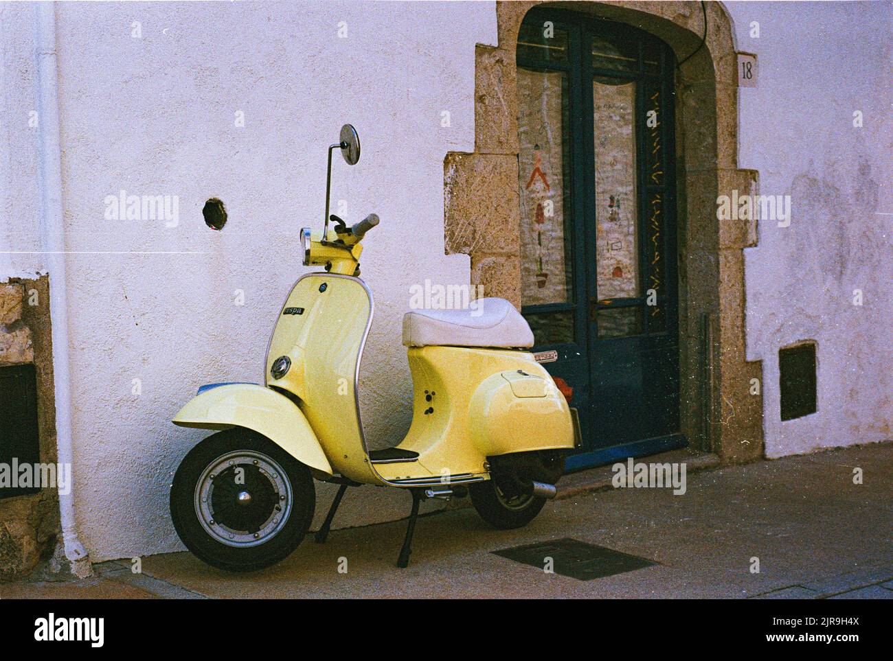 An Italian yellow Vespa scooter parked in front of a white building Stock Photo