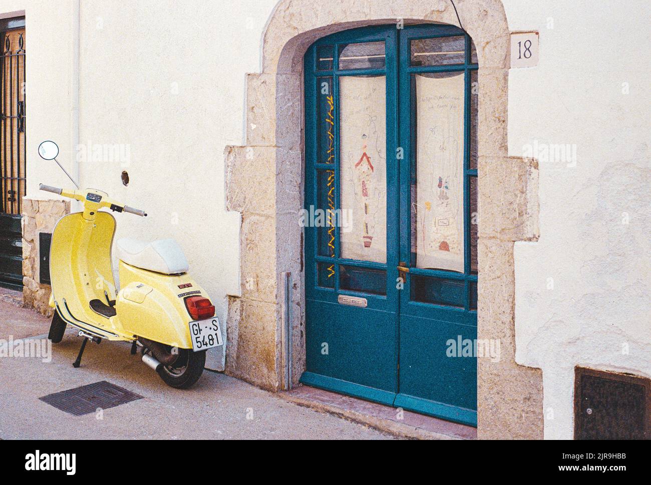 An Italian yellow Vespa scooter parked in front of a white building with a blue door Stock Photo