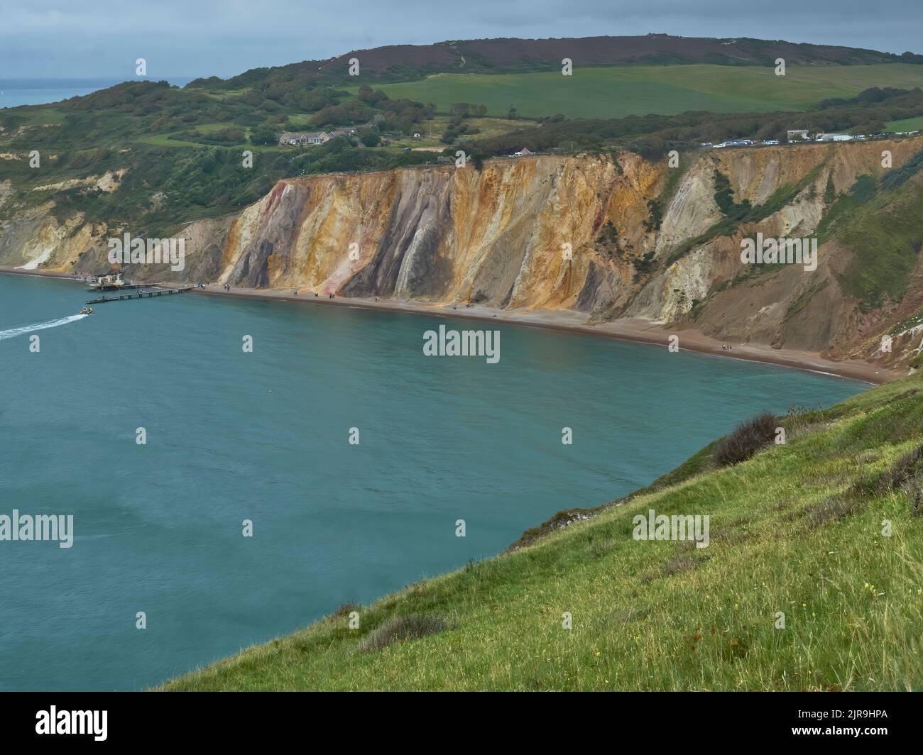 The curious multi-coloured cliffs and beach at Alum Bay - stained by oxidised mineral deposits - with the sea lapping gently at the shore. Stock Photo