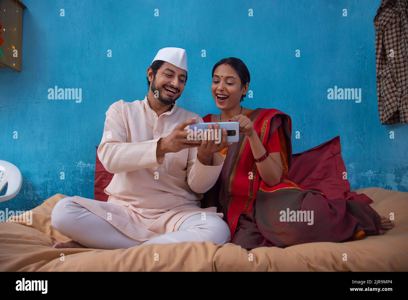 Maharashtrian couple using smartphone together while sitting on cot at home Stock Photo