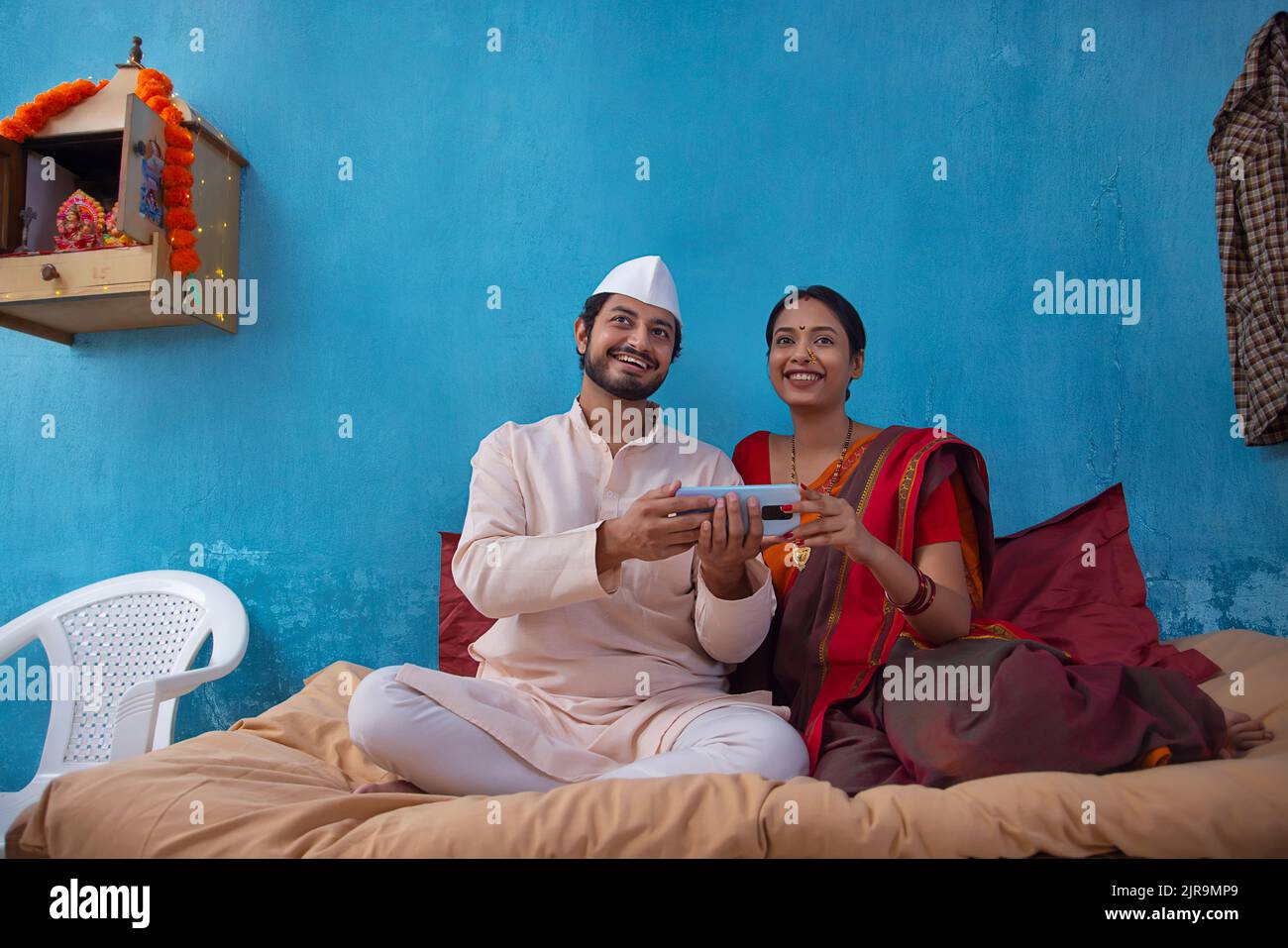 Maharashtrian couple using smartphone together while sitting on cot at home Stock Photo