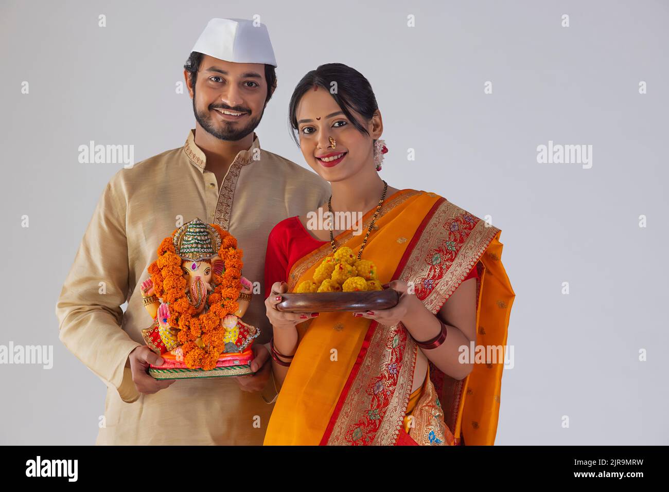 Portrait of Maharashtrian couple carrying statue of Lord Ganesh and plate of sweet food Stock Photo