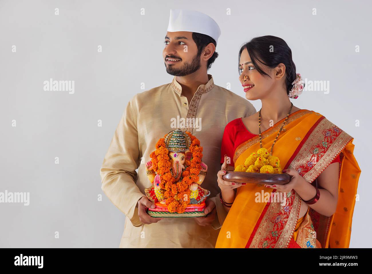 Maharashtrian couple carrying statue of Lord Ganesh and plate of sweet food Stock Photo