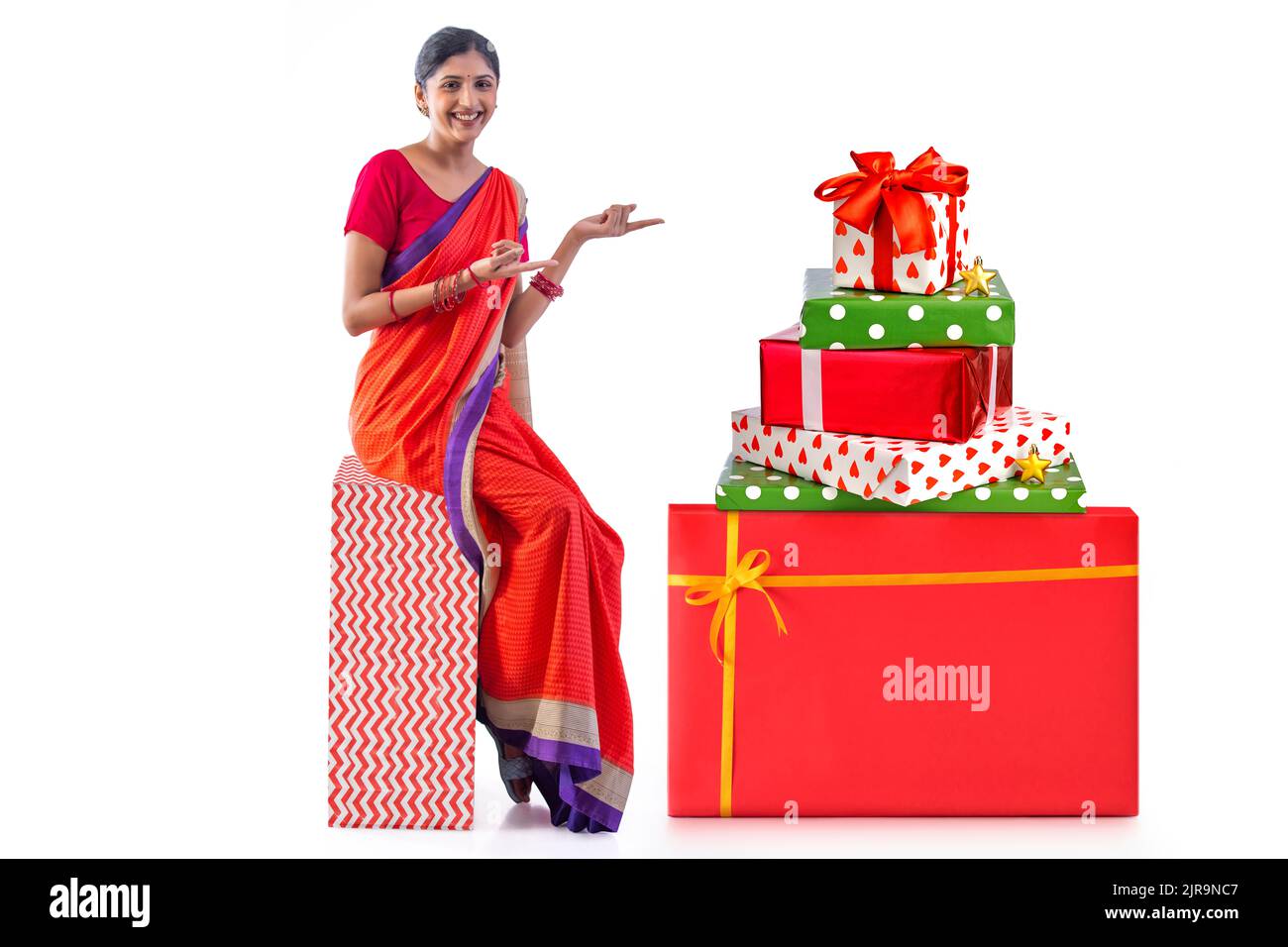 Cheerful woman sitting on gift box against white background Stock Photo