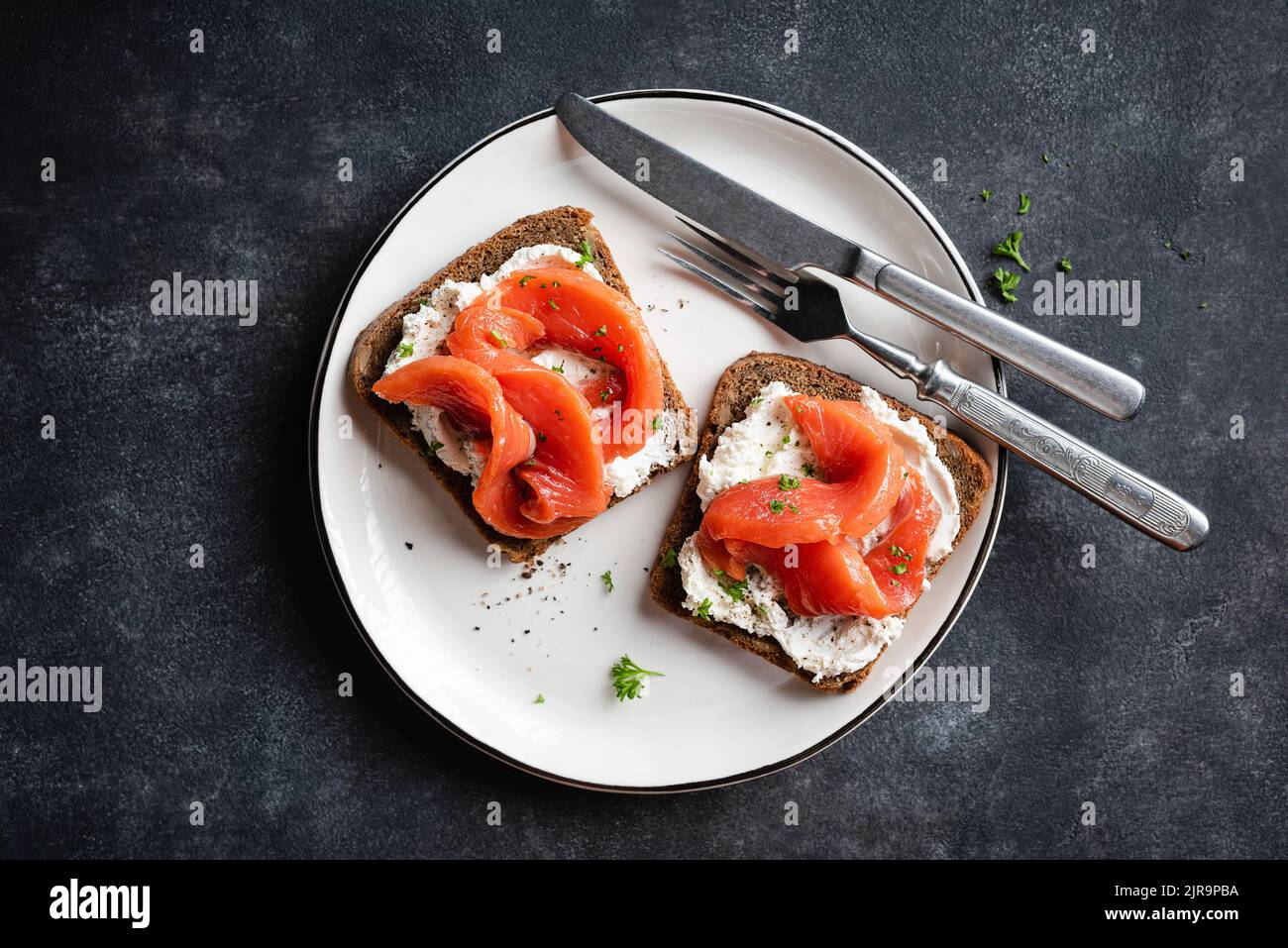 Rye bread with cream cheese and smoked salmon toast on plate, black stone background. Tasty red fish toast or open sandwich Stock Photo