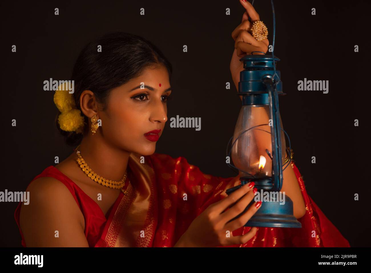 Close-up of a woman in red sari holding lantern against dark background Stock Photo