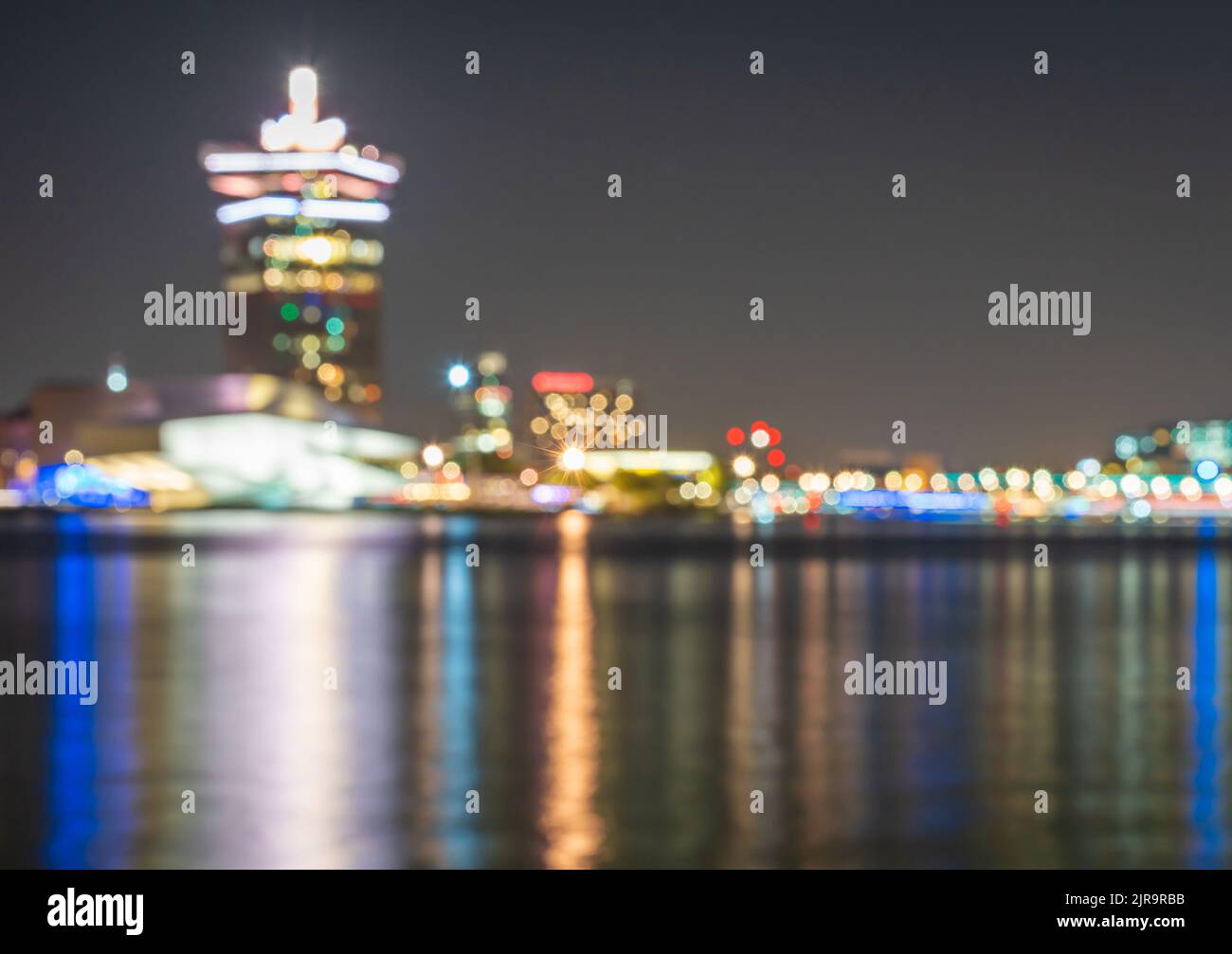 Defocused skyline of Amsterdam at night, blurred lights of traffic and modern buildings around IJ river nearby central station Stock Photo