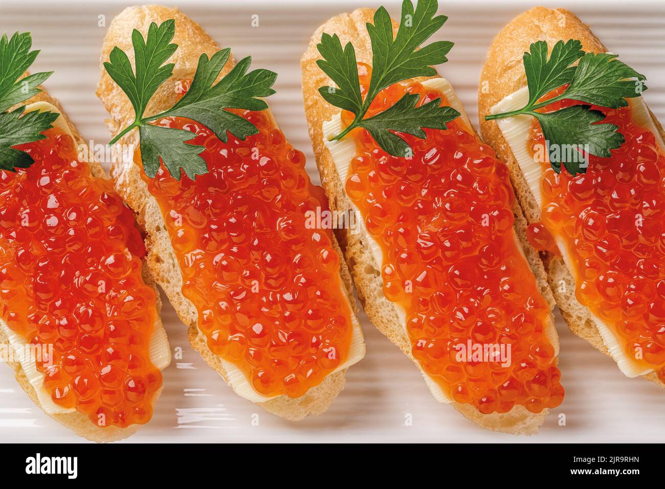Delicious sandwiches with salmon caviar and parsley on a plate. Close-up of trout red caviar on a slice of french baguette with butter. Gourmet. Stock Photo