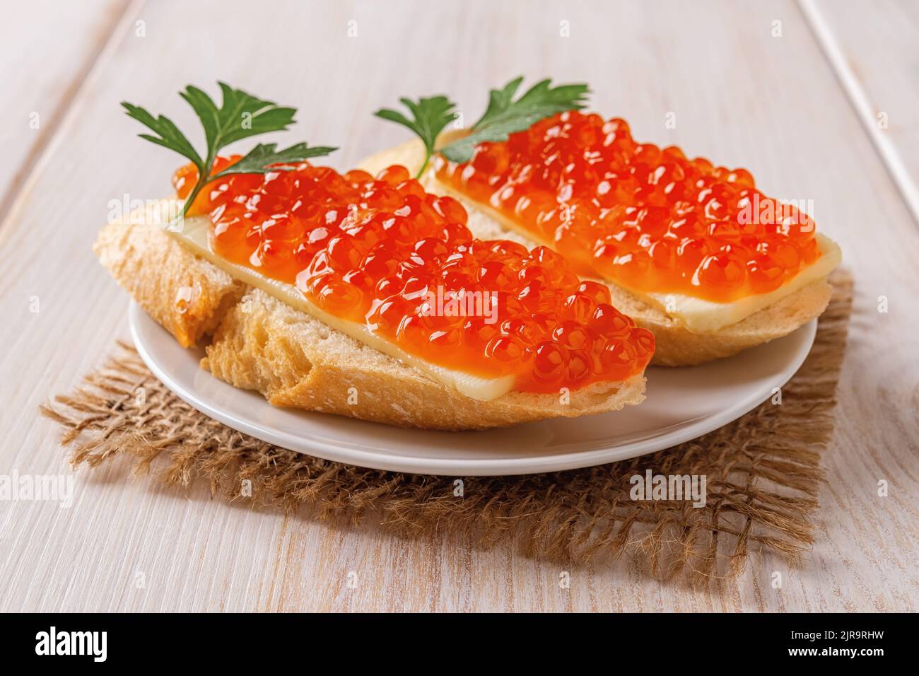 Two sandwiches with red caviar on a saucer over wooden table. Gourmet appetizer of trout caviar on a french baguette slice with butter.  Close-up. Stock Photo