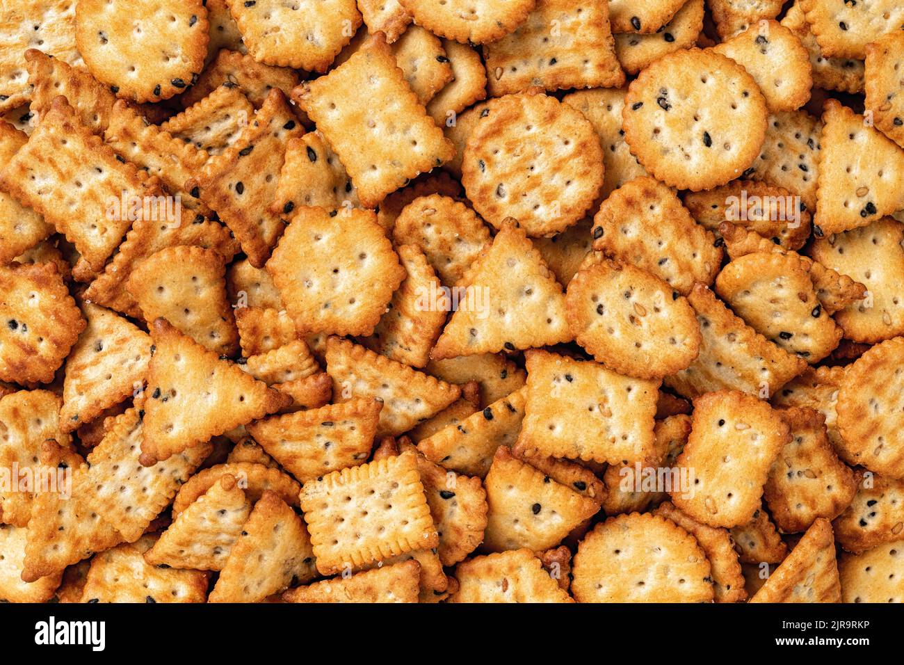 Saltine cracker background. Texture of salty crackers with black and white sesame seeds. Various shaped sesame cookies macro. Ready to eat snack macro Stock Photo