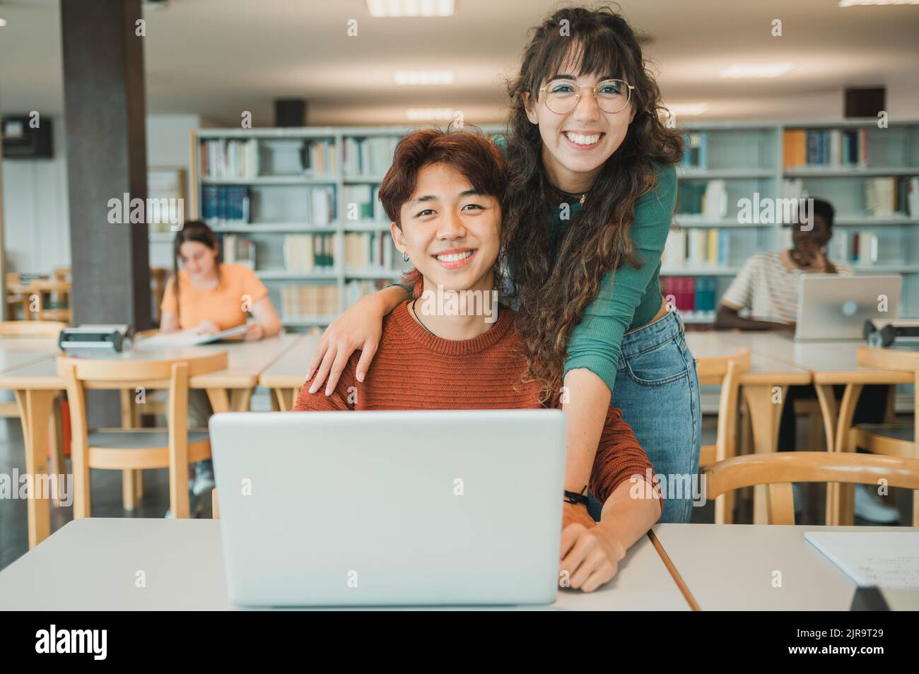 Cheerful diverse students with laptop in library Stock Photo