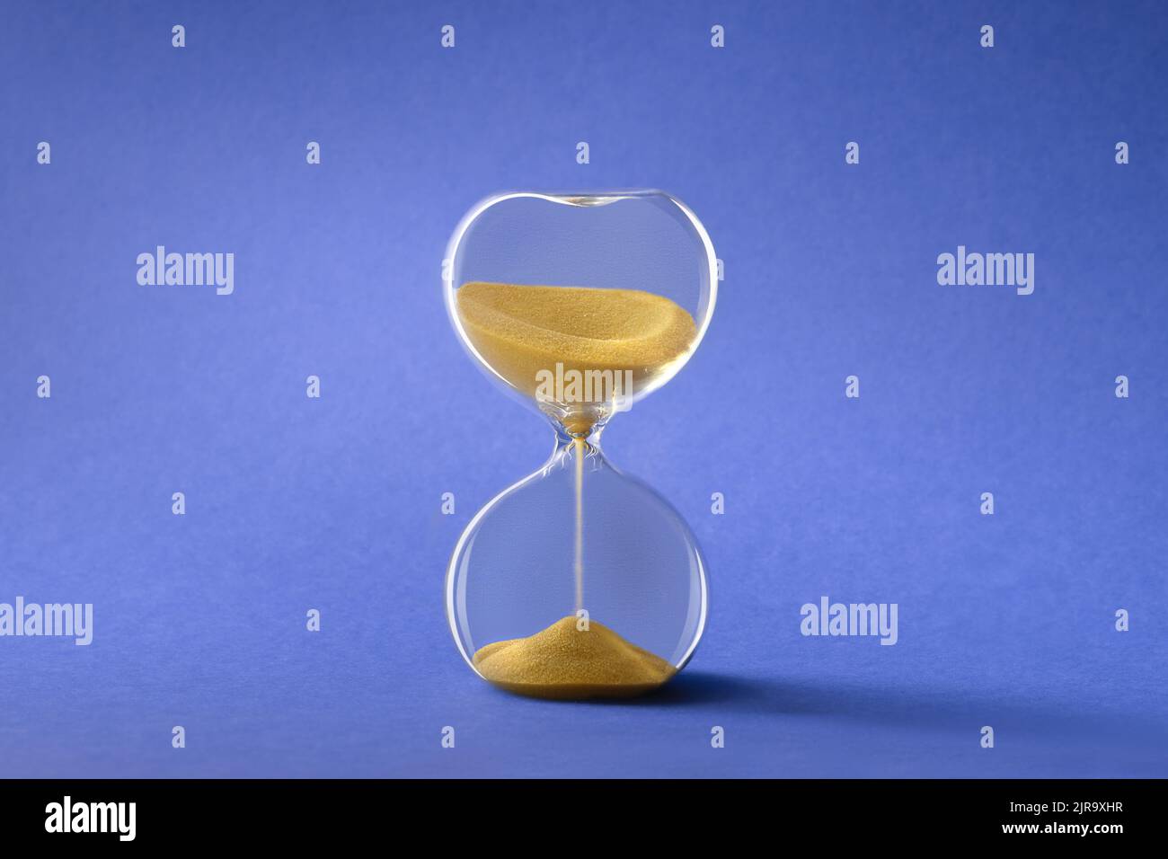 Hourglass, also known as sandglass or sand timer, golden on blue paper background Stock Photo