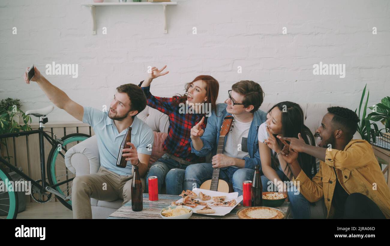 Happy student friends taking selfie and posing while have party with beer and pizza in shared accommodation Stock Photo