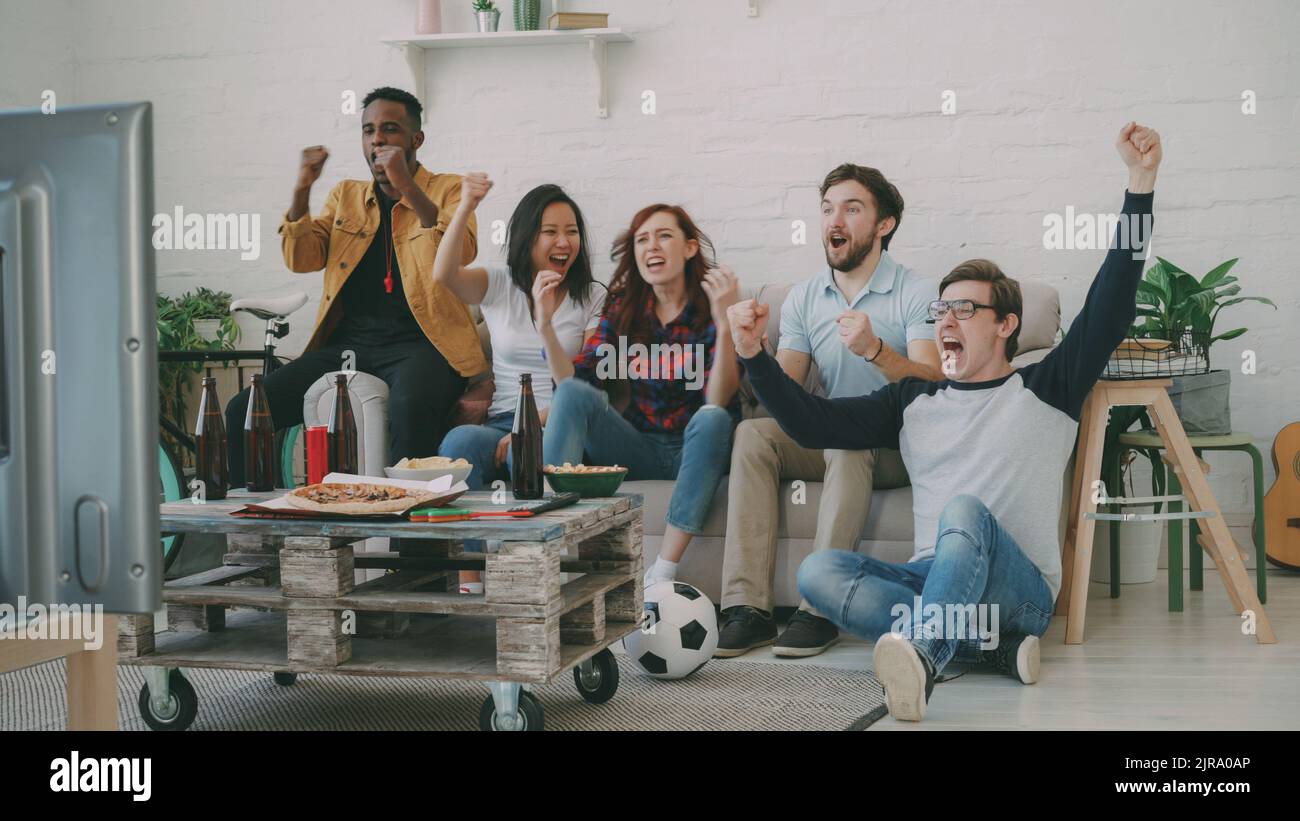 Group of happy friends watching sports game on TV at home indoors. They