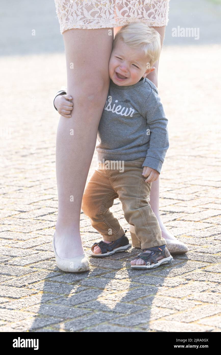 Sad caucasian blonde little boy hugging her mother legs. High quality photo Stock Photo