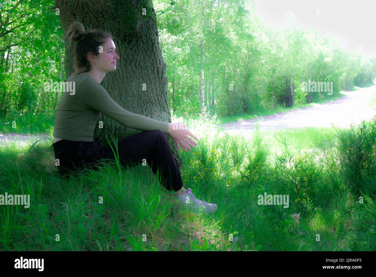 Young brunette woman sitting in green forest enjoys the silence and beauty of nature watching over a blue forest lake on a summer day. High quality photo Stock Photo