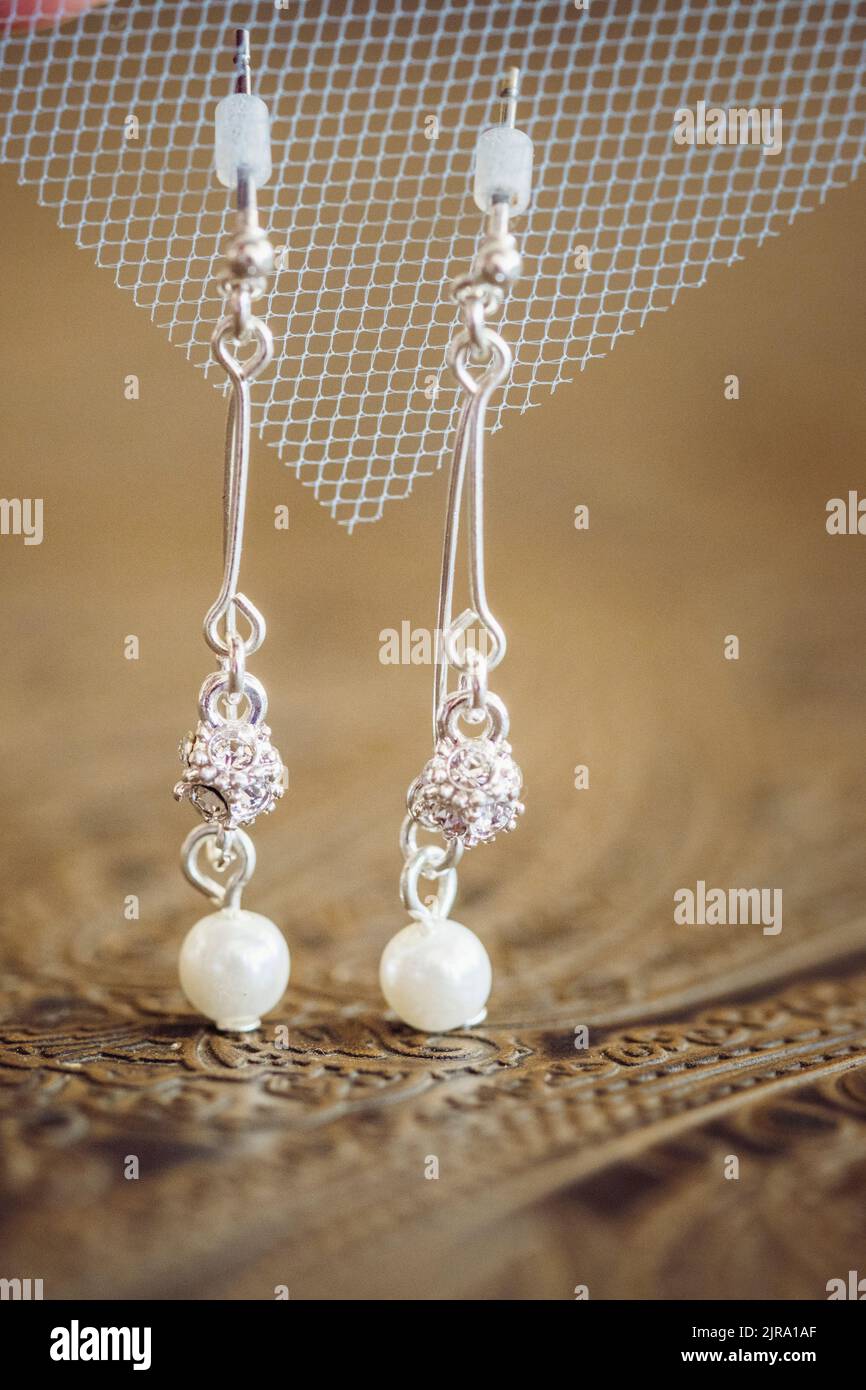 A vertical shot of bridal white pearl earrings hanging from mesh fabric Stock Photo