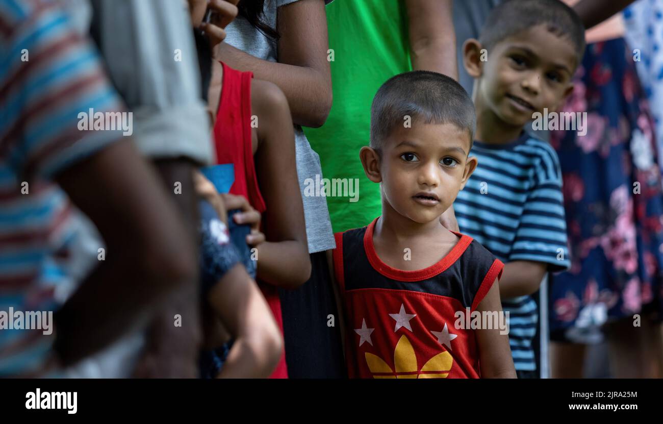 Child waiting to receive food parcel from a community almsgiving eagerly peeking: Galle, Sri Lanka 30th July 2022 Stock Photo