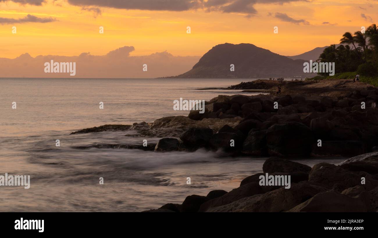 Long exposure sunset photo of the coast on the west side of Oahu with the Waianae Mountains in the distance. Stock Photo