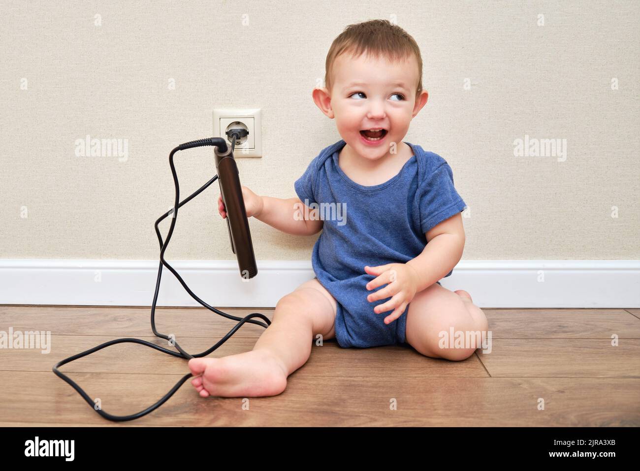 Toddler baby is playing with hot curling tongs at the power outlet