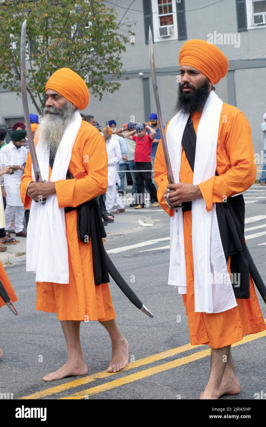 Two devout Sikh men dressed in orange and carrying swords march in the Nagar Kirtan Parade in Queens, New York City. Stock Photo