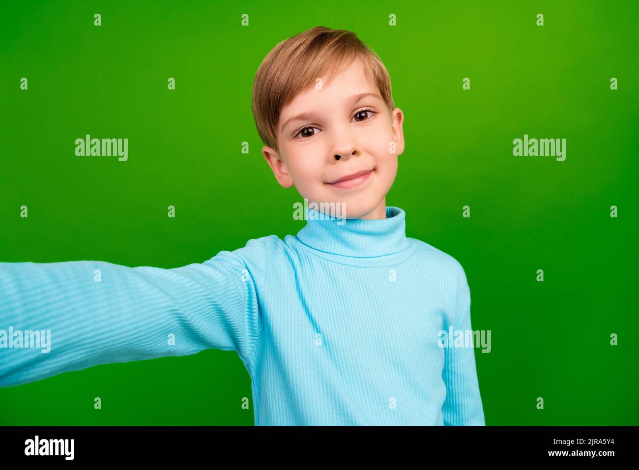 Photo of cute cheerful little grandson dressed teal turtleneck recoding self video isolated green color background Stock Photo