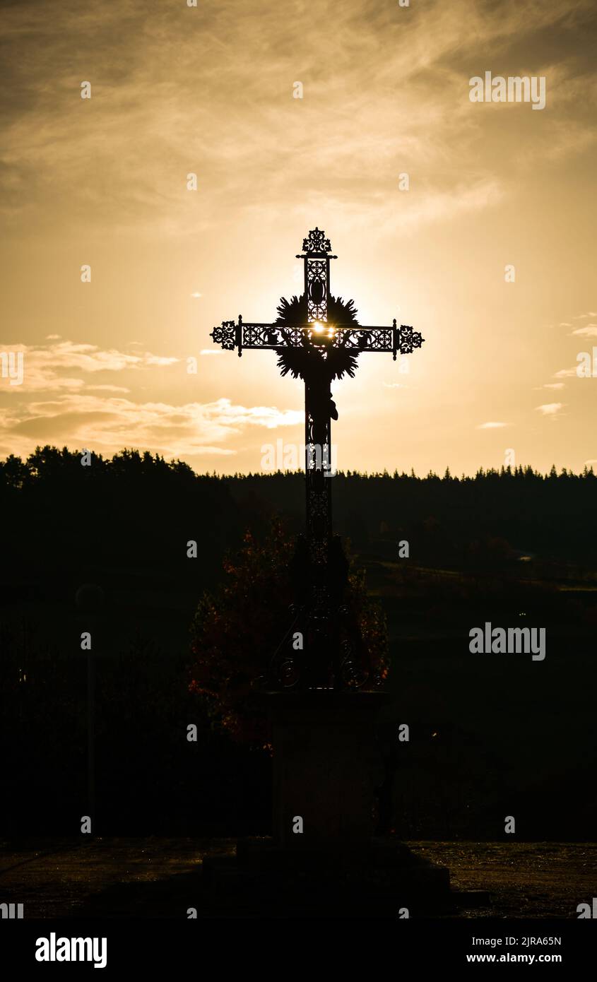 Chanaleilles (south of France): sunray through a wrought iron cross in the village square, at sunset Stock Photo