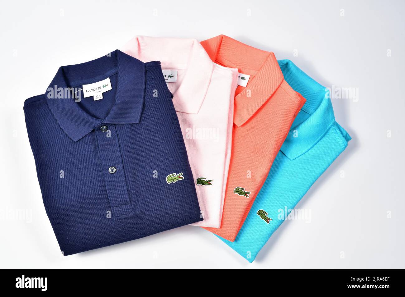 Classical Lacoste polo shirts in various colours, dark blue, pink, range and pale blue, adorned with a green embroidered contrasting crocodile design Stock Photo