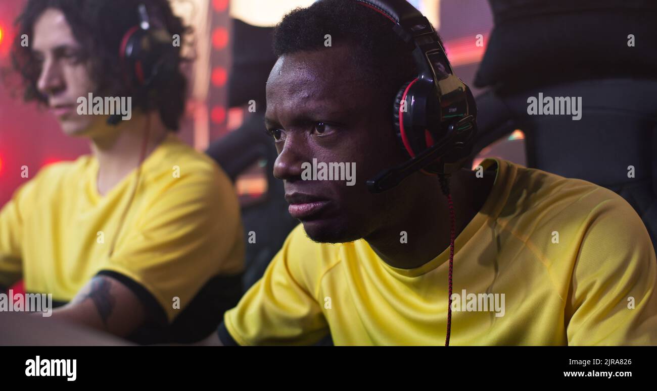 Concentrated esportsman gamer speaking with teammates and playing video game battle during professional championship Stock Photo